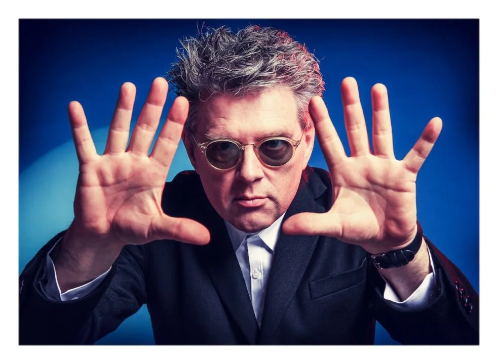 Tom Bailey holding up hands with blue background